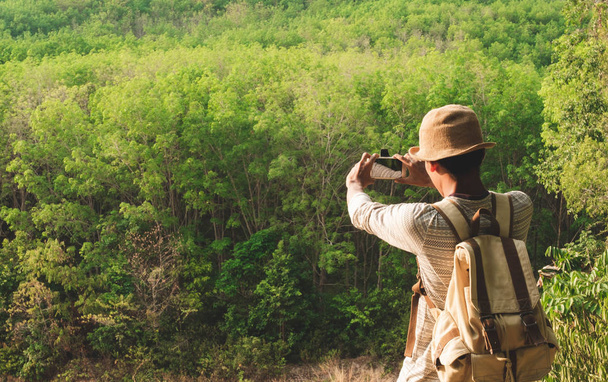 Мужчина с рюкзаком фотографирует концепцию летних отпусков на природе в одиночестве
 - Фото, изображение