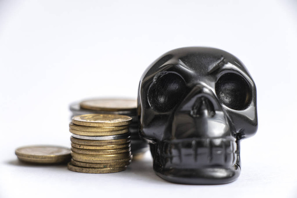 figura de crânio de pedra ao lado de pilhas de pequenas moedas
 - Foto, Imagem