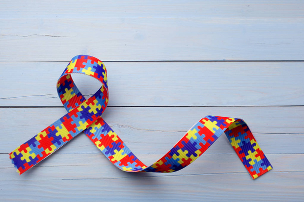 World Autism awareness and pride day or month with Puzzle pattern ribbon on blue wooden background. - Photo, Image