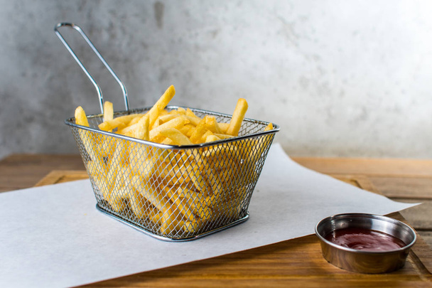 картофель фри в железной сетке и соус на деревянном столе серый фон
 - Фото, изображение