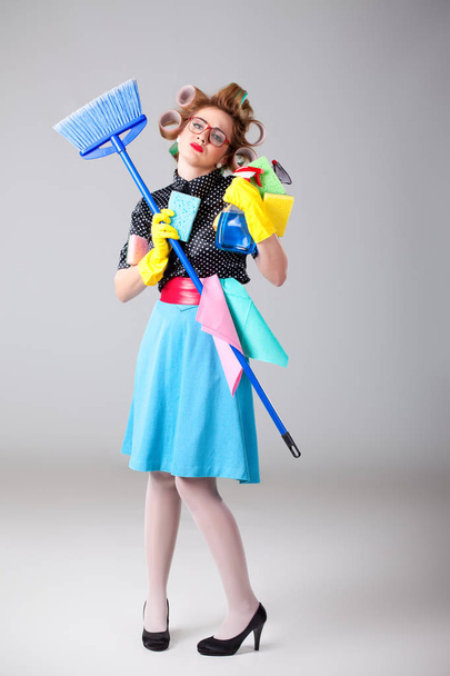 Desperate and tired funny looking housewfe holding many cleaning equipment - 写真・画像