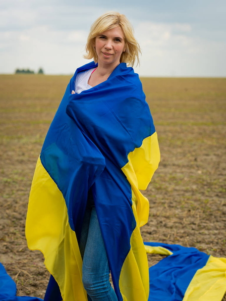 Young amazing beautiful girl with a huge Ukrainian flag on the field. Ukraine's Independence Day. - Photo, Image