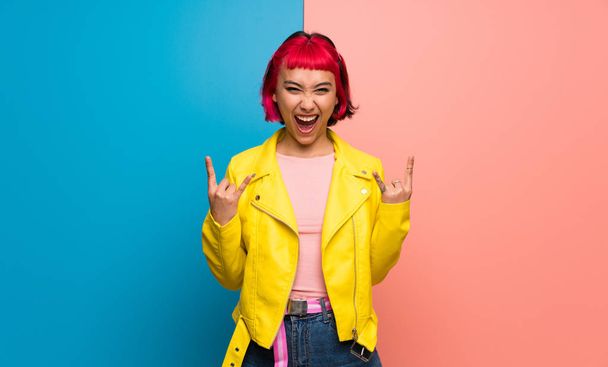 Young woman with yellow jacket making rock gesture - Foto, imagen
