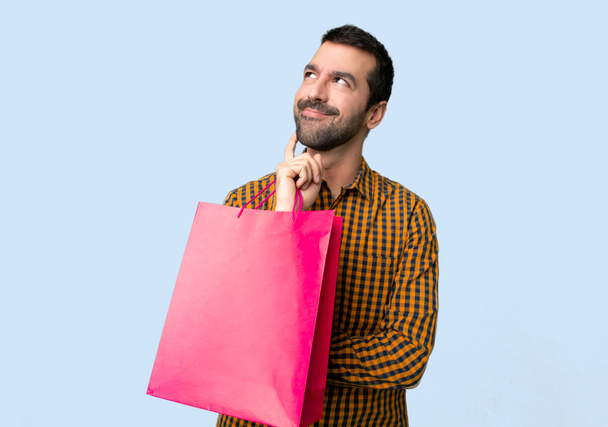 Hombre con bolsas de compras pensando en una idea mientras mira hacia arriba en el fondo azul aislado
 - Foto, imagen
