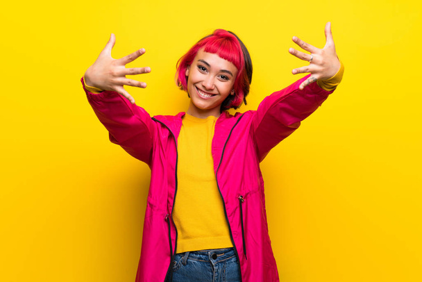 Молода жінка з рожевим волоссям над жовтою стіною рахуючи десять пальцями
 - Фото, зображення