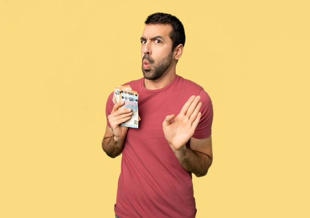 Man taking a lot of money making stop gesture with both hands on isolated yellow background - Photo, Image