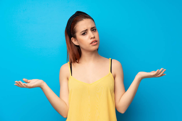 Young redhead woman over blue background unhappy because not understand something - Фото, изображение
