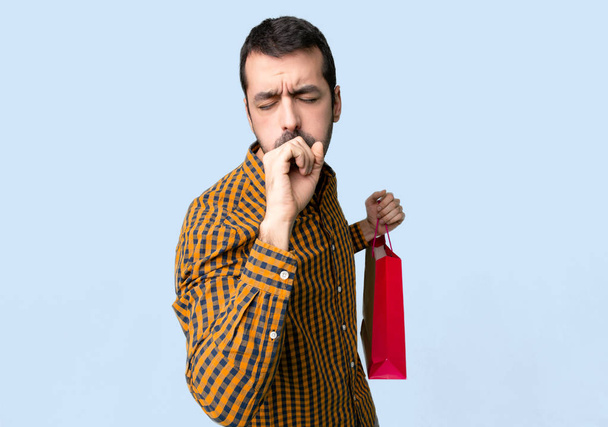 Man with shopping bags is suffering with cough and feeling bad on isolated blue background - Photo, Image