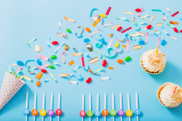 birthday hat with confetti and cupcake on blue paper background - Φωτογραφία, εικόνα