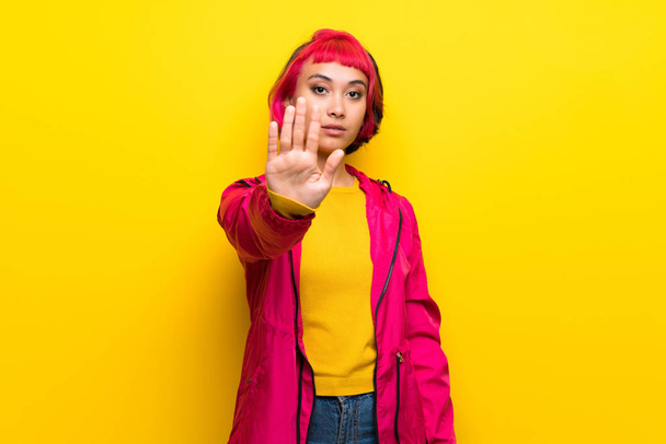 Mujer joven con el pelo rosa sobre la pared amarilla haciendo gesto de parada
 - Foto, Imagen