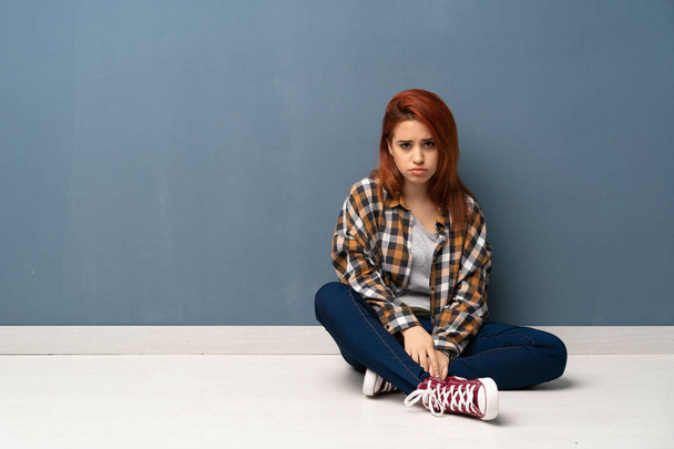 Young redhead woman sitting on floor with sad and depressed expression - Photo, Image