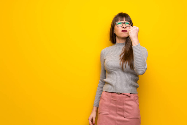 Mujer con gafas sobre pared amarilla con gesto de enojo
 - Foto, Imagen