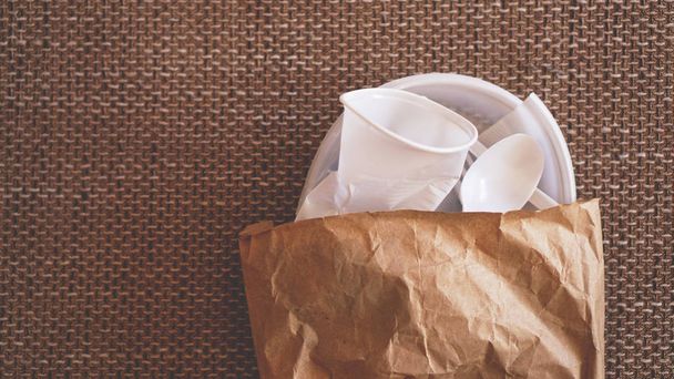 White crumpled plastic dishes in a paper packet on beige background - Foto, afbeelding