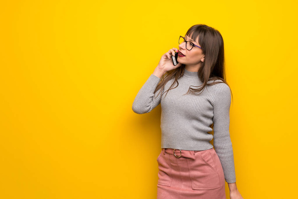 Cep telefonu ile bir konuşma tutmak sarı duvarın üzerinden gözlüklü kadın - Fotoğraf, Görsel