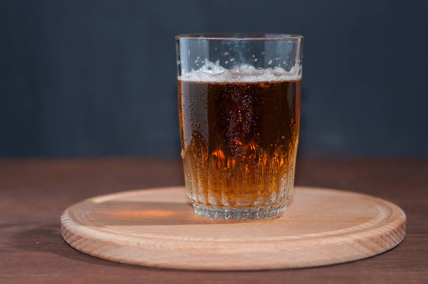 Cerveja leve em um copo de vidro alto em um suporte de madeira em fundo de madeira marrom
 - Foto, Imagem
