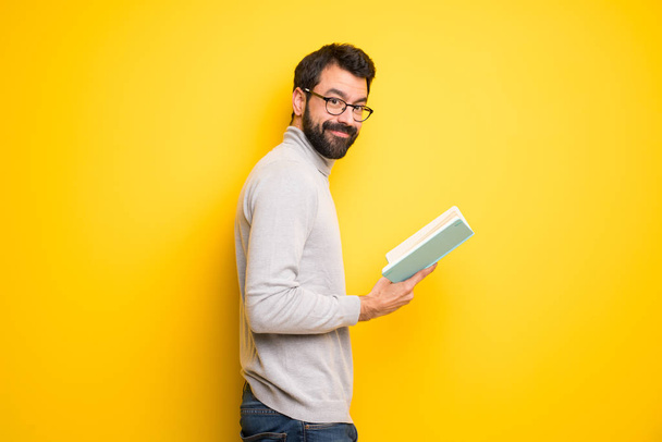 Hombre con barba y cuello alto sosteniendo un libro y disfrutando de la lectura
 - Foto, Imagen