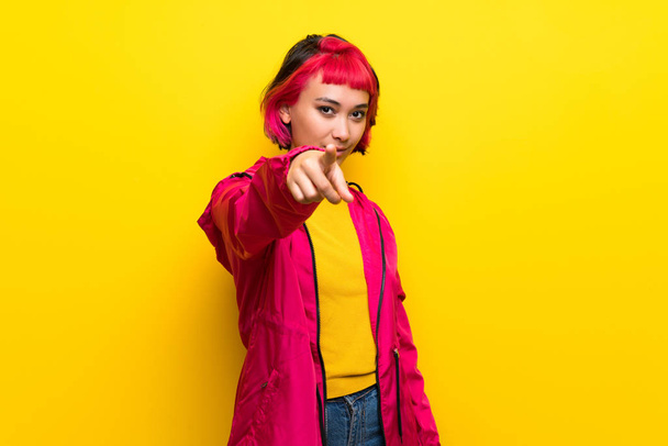 Fiatal nő, rózsaszín haj felső sárga fal pontok ujj nálad, magabiztos kifejezés - Fotó, kép