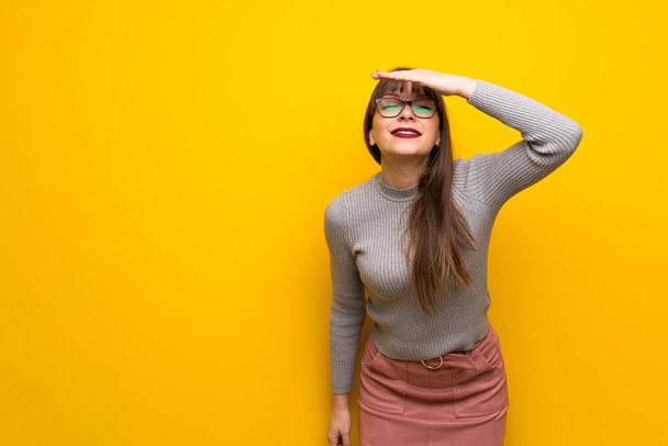 Woman with glasses over yellow wall looking far away with hand to look something - Photo, Image