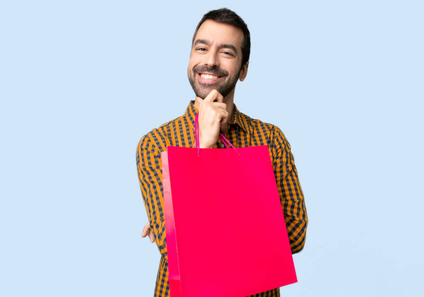 Mann mit Einkaufstaschen lächelt und blickt nach vorne mit selbstbewusstem Gesicht auf isoliertem blauem Hintergrund - Foto, Bild