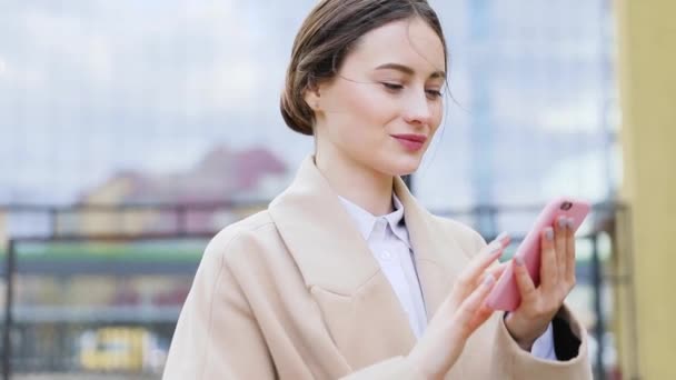 closeup of beautiful young business Asian woman with smartphone texting messenger with skyscrapers in the background - Záběry, video