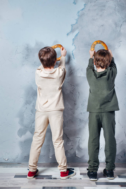 Little twin boys playing and dreaming of becoming a spaceman. Portrait of funny kids with bagels on gray wall - Foto, immagini