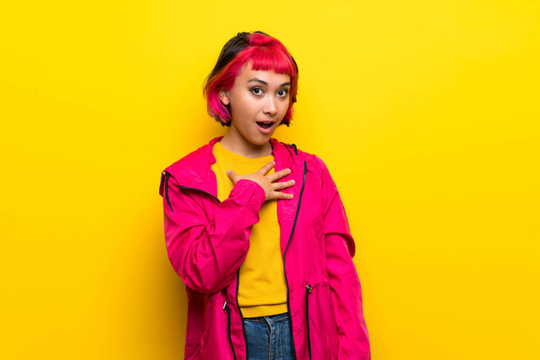 junge Frau mit rosa Haaren über gelber Wand überrascht und schockiert, während sie nach rechts schaut - Foto, Bild