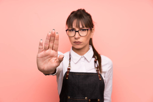 Joven camarera sobre fondo rosa haciendo gesto de stop con su mano
 - Foto, Imagen