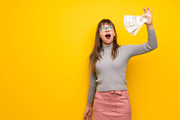 Γυναίκα με τα γυαλιά πάνω από κίτρινο τοίχο λαμβάνοντας πολλά χρήματα - Φωτογραφία, εικόνα