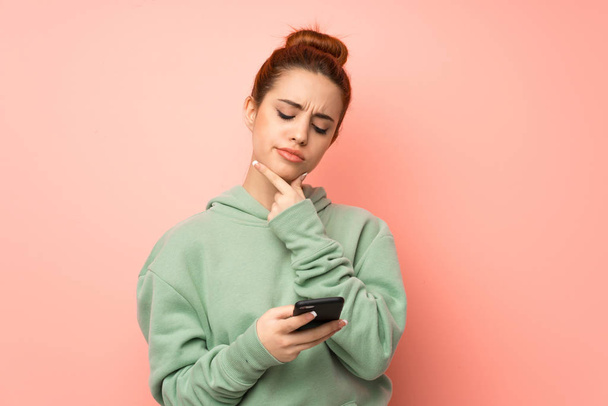Young redhead woman with sweatshirt thinking and sending a message - Photo, Image