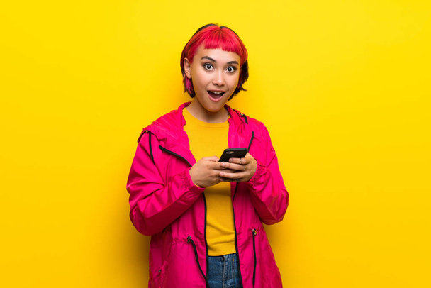 Giovane donna con i capelli rosa sopra il muro giallo sorpreso e l'invio di un messaggio
 - Foto, immagini