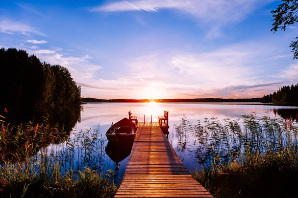 Wooden pier with fishing boat at sunset on a lake in Finland - Fotoğraf, Görsel