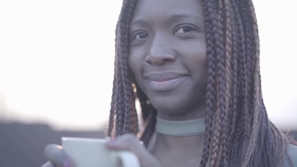 Close up portrait of confident african american young black smiling woman with hot cup of coffee on the street. Slow motion - Πλάνα, βίντεο