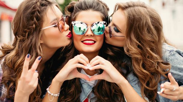 hinreißende Teenager mit Sonnenbrille küssen ihren Freund lächelnd in die Kamera mit Herzensgeste. - Foto, Bild