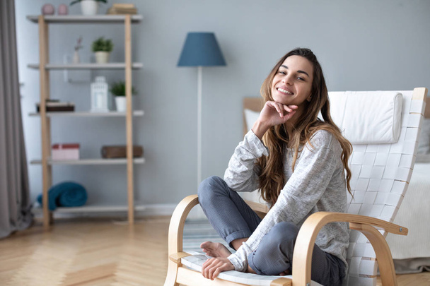 Smiling millennial girl sitting in a cozy chair at home.  - Foto, afbeelding