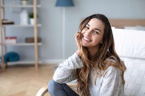 Smiling millennial girl sitting in a cozy chair at home.  - Foto, Bild