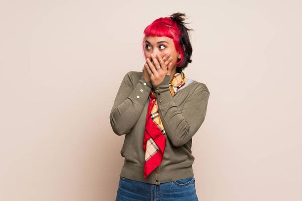 Young woman with pink hair over yellow wall covering mouth and looking to the side - Fotoğraf, Görsel
