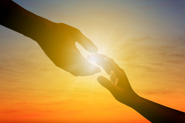 Man bereiken voor vrouw hand bij zonsondergang buitenshuis, close-up. Help begrip - Foto, afbeelding