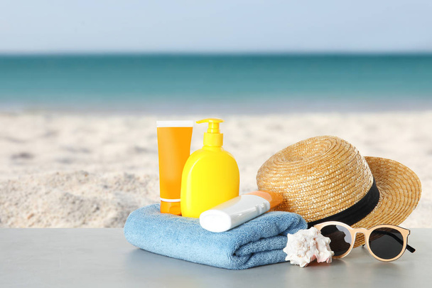 Set with different bottles of sun protection body cream and beach accessories on table against seascape. Space for design - Foto, Imagen