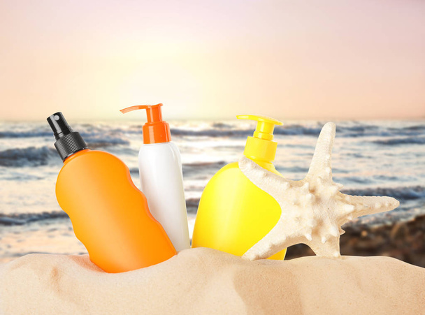 Set with different bottles of sun protection body cream and starfish on sand beach. Space for design  - Фото, зображення