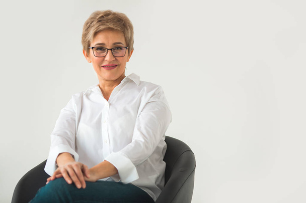 portrait of stylish aged woman in glasses in white shirt and short haircut on white background - Foto, Imagem