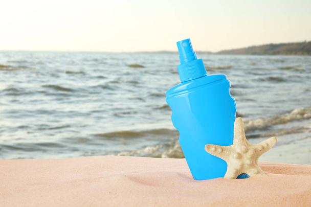 Bottle of sun protection body cream and starfish on sand beach. Space for design  - Фото, изображение