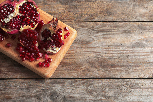 Board with ripe pomegranates and seeds on wooden background, top view. Space for text - 写真・画像