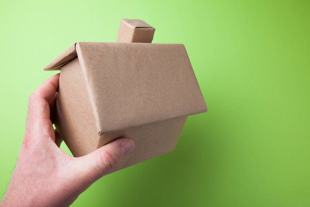 A small cardboard house in his hand. Green background. - Φωτογραφία, εικόνα