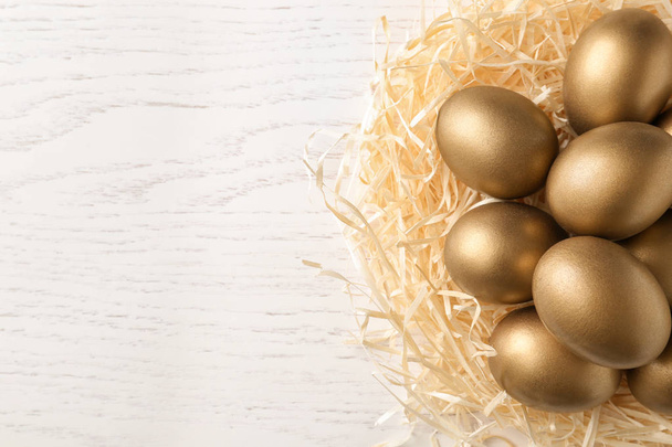 Golden eggs in nest on wooden background, top view with space for text - Фото, зображення