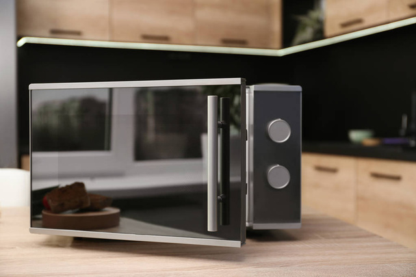 Open modern microwave oven on table in kitchen - Foto, afbeelding