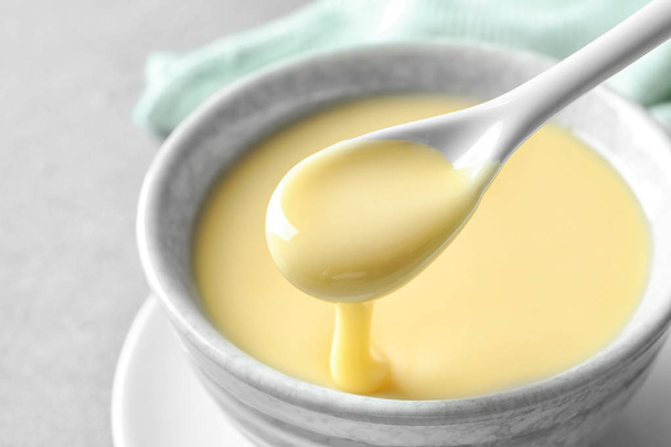 Spoon of pouring condensed milk over bowl on table, closeup. Dairy products - Photo, image