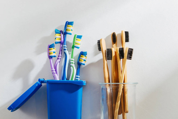 Eco friendly bamboo toothbrushes in glass and plastic toothbrushes in trash bin. Zero waste, plastic free, ecology concept.  - 写真・画像