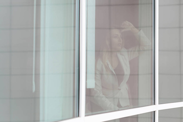 rom behind the glass. a modern business woman looks out the window of the office - 写真・画像