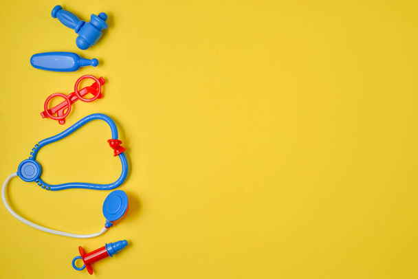 Top view of children's set stethoscope, syringe, glasses, hammer and thermometer on yellow background. Flat lay and copy space. Medical Concept - 写真・画像