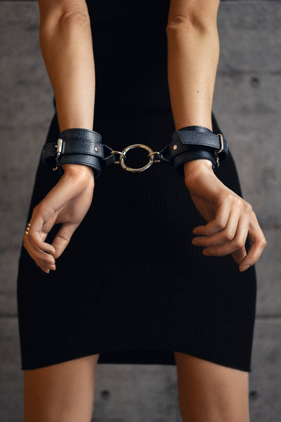 Close up back view of female hands in black leather handcuffs - Фото, изображение